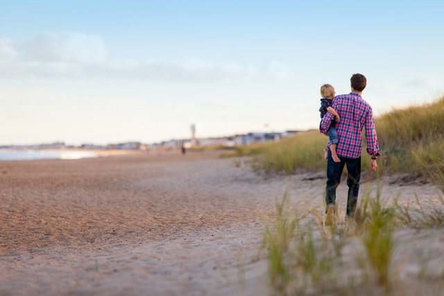 Adult holding a toddler-aged child as they walk outdoors, presumably in conversation