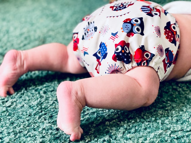 infant in prone position aka "tummy time." the baby is only visible below the waist. umbilical hernia not visualized. baby wears a cloth diaper.