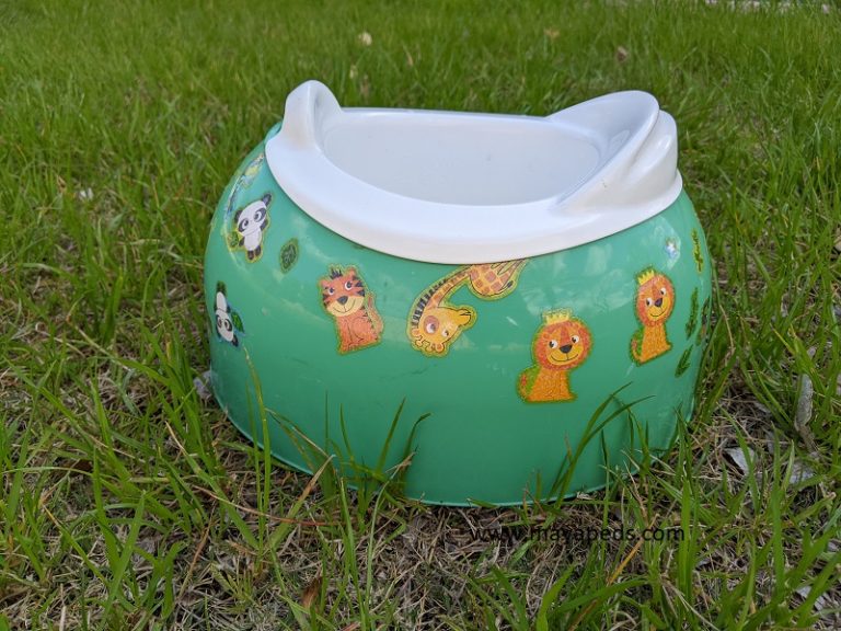 green child's potty chair with white insert, covered with stickers. the potty is sitting in grass outside. this is one of the more important potty learning supplies.