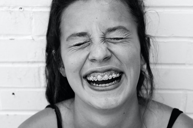 black and white photo of a young person smiling with braces visible on teeth. eyes are closed.