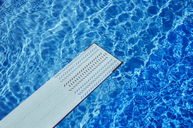 image of the end of a diving board extending over pool water