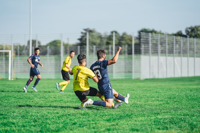 image of 4 adolescent soccer players in yellow and blue jerseys playing on the field. 2 opposing players are falling, at a risk for injury, such as an ACL tear