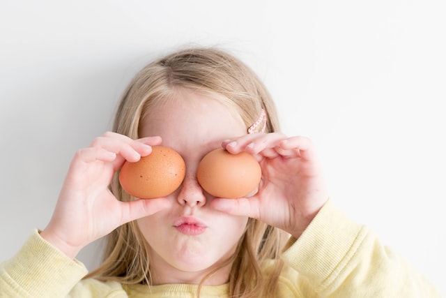photo of young child holding 2 chicken eggs over her eyes, making a silly face